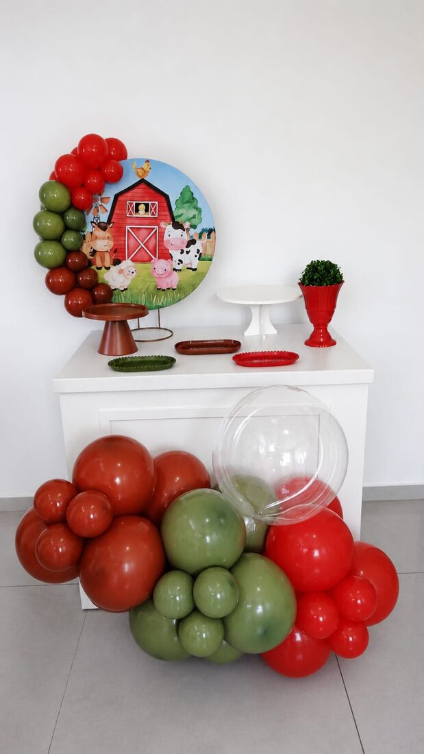 Festa na mesa com tema fazendinha, guirlanda de balões verdes e vermelhos e painel de celeiro